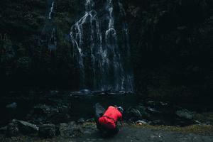 lato posteriore del fotografo in t-shirt rossa con la moderna fotografia della fotocamera che cattura il paesaggio della cascata. foto