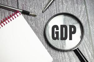 testo gdp su lente d'ingrandimento e penna, blocco note su sfondo di legno foto