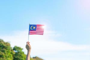 mano che tiene la bandiera della Malesia su sfondo blu cielo. settembre festa nazionale della Malesia e agosto giorno dell'indipendenza foto