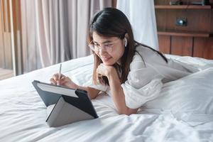 donna felice che usa tablet per i social media, giovane donna che guarda film sul pad del computer sul letto di casa. tecnologia, rete, shopping online, e-commerce, stile di vita e concetto di comunicazione digitale foto