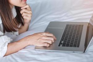 donna felice che usa il laptop per lavoro, riunione femminile online dal computer portatile sul letto. tecnologia, rete, lavoro da casa, stile di vita e concetto di comunicazione digitale foto