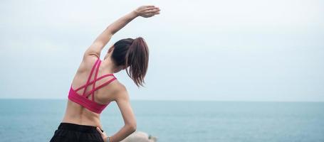 giovane donna fitness in abbigliamento sportivo che allunga il corpo contro la vista sull'oceano, esercizio sano della donna al mattino. concetti di allenamento, benessere e vita lavorativa foto