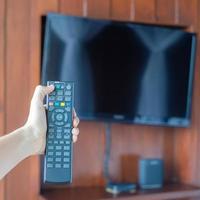 mano usando il telecomando per regolare la smart tv all'interno della stanza moderna a casa o in un hotel di lusso foto