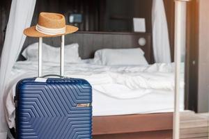 bagagli blu con cappello in una moderna camera d'albergo dopo l'apertura della porta. tempo per viaggiare, servizio, viaggio, viaggio, vacanze estive e concetti di vacanza foto