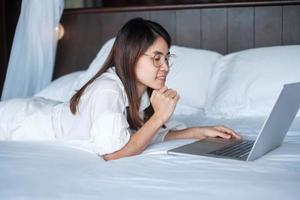 donna felice che usa il laptop per lavoro, riunione femminile online dal computer portatile sul letto. tecnologia, rete, lavoro da casa, stile di vita e concetto di comunicazione digitale foto