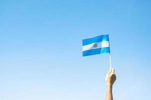 mano che tiene la bandiera dell'argentina sullo sfondo della natura. 9 luglio del giorno dell'indipendenza, 25 maggio del giorno della rivoluzione e felici concetti di celebrazione foto