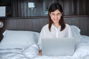 donna felice che usa il laptop per lavoro, riunione femminile online dal computer portatile sul letto. tecnologia, rete, lavoro da casa, stile di vita e concetto di comunicazione digitale foto