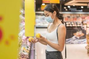 donna asiatica che indossa una maschera per il viso che fa shopping nel supermercato. concetto di sicurezza e pandemia di coronavirus. nuovo stile di vita normale. foto