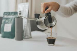 giovane donna felice che usa la moka per fare il caffè a casa. donna asiatica che versa il caffè in una tazza. foto