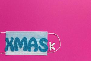 maschera protettiva medica su sfondo rosa. iscrizione natale. carta di natale e capodanno, banner, concetto pubblicitario. vista dall'alto foto, minimalismo, copia spazio. medico in modo piatto. foto di alta qualità