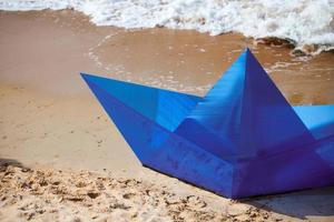barca di carta blu origami sulla spiaggia sabbiosa per il concept design, bella nave di carta sulla riva, primo piano foto