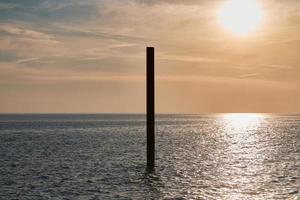 grande pilastro di costruzione in acciaio arrugginito nel mare blu con onde calme al tramonto, parte di edificio abbandonata foto