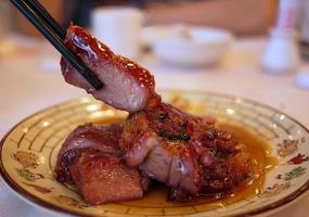 bacchette con vista laterale ravvicinata che tengono un pezzo di succoso e delizioso barbecue in stile cantonese di maiale arrosto foto