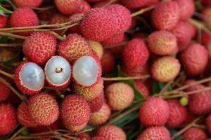 litchi, litchi freschi e pelati che mostrano la buccia rossa e la polpa bianca con foglia verde. foto