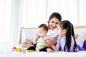 donna impegnata che si prende cura del suo bambino e della sua piccola figlia e lavora da casa con il laptop foto