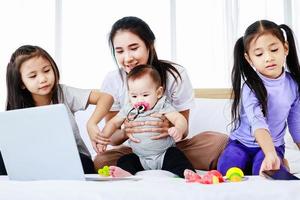 concetto di mamma single impegnato, madre che lavora al laptop e si prende cura del suo bambino e della sua piccola figlia foto