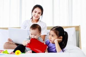 donna asiatica impegnata che si prende cura del suo bambino e della sua piccola figlia e lavora da casa con il laptop. super-mamma foto