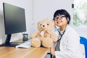 un bambino vestito da medico si siede ed esamina un orsacchiotto in ospedale. foto