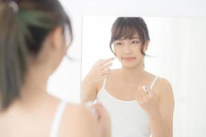 bella giovane donna asiatica sorridente con cosmetici per la cura della pelle uso carta assorbente olio sul viso specchio in camera, bellezza asia ragazza pulire e trucco detergente con tessuto, pulire sul concetto facciale. foto