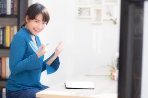 bella scrittrice della giovane donna asiatica del ritratto che scrive sul taccuino o sul diario con felice ed eccitato, la ragazza dell'asia di stile di vita che pianifica il lavoro e il successo, l'istruzione e il concetto di affari. foto