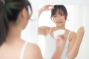 bella giovane donna asiatica sorridente con cosmetici per la cura della pelle uso carta assorbente olio sul viso specchio in camera, bellezza asia ragazza pulire e trucco detergente con tessuto, pulire sul concetto facciale. foto