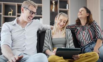 felice famiglia caucasica che utilizza tablet, laptop, telefono per giocare a guardare film, rilassarsi a casa per il concetto di stile di vita tecnologico foto
