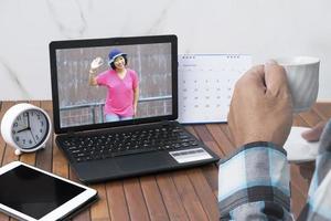 primo piano uomo che beve caffè caldo e fa una videochiamata con la sua ragazza asiatica sul computer portatile a casa foto