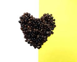 chicchi di caffè tostati a forma di cuore variazione di semi marroni e scuri su metà sfondo bianco e giallo foto
