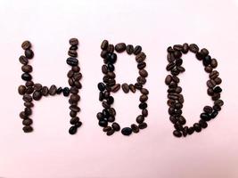 scritte di buon compleanno con chicchi di caffè tostati variazione di semi marroni e scuri su sfondo rosa pastello foto