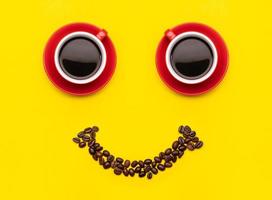 tazza di caffè e chicchi di caffè con il concetto di faccia sorridente, vista dall'alto su sfondo giallo. per il concetto di mattina felice foto
