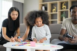 famiglia asiatico-afroamericana che si rilassa, chiacchiera, dipinge e si diverte in vacanza nel soggiorno di casa foto