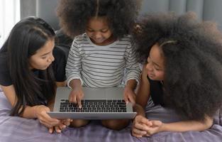 la famiglia afroamericana asiatica usa un laptop per navigare in Internet e fare acquisti online. sul letto in camera da letto in vacanza. foto