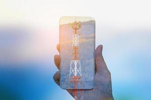 tenere in mano smartphone mobile doppia esposizione con torre delle telecomunicazioni foto