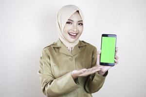 lavoratore governativo sorridente che mostra uno schermo vuoto su uno smartphone. un giovane pns musulmano asiatico che indossa l'uniforme cachi e l'hijab. foto