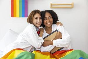 coppia dello stesso sesso matrimonio di razze diverse che tengono la bandiera arcobaleno lgbtq per il mese dell'orgoglio per promuovere l'uguaglianza e le differenze di omosessualità e discriminazione foto