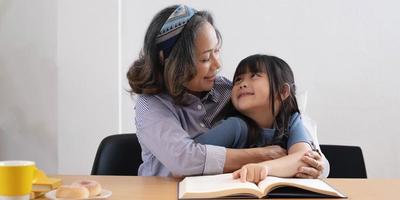 felice famiglia asiatica nonna che legge al libro del nipote della nipote a casa foto