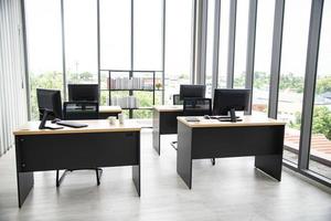 design degli interni dell'ufficio moderno con notebook monitor da tavolo e grande finestra di vetro intorno alla stanza senza persone foto