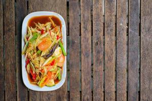 insalata di papaia piccante con granchio salato e pesce fermentato sullo sfondo di legno. foto