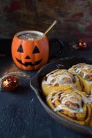 padella in ghisa di zucca di halloween involtini alla cannella conditi con glassa bianca con bevanda in tazza di zucca foto