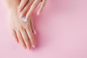 una giovane donna si sta applicando la crema sulle mani. concetto di cura del corpo e della spa su uno sfondo rosa. immagine per la pubblicità. foto