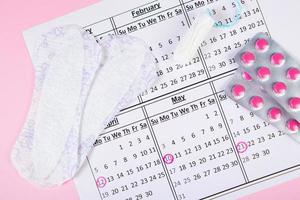 calendario delle mestruazioni. assorbenti, tamponi, pillole su sfondo rosa. foto