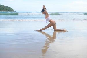 giovane donna asiatica in bikini che fa yoga sul concetto di spiaggia, salute e meditazione foto