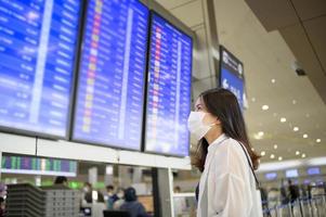 una donna viaggiatrice indossa una maschera protettiva nell'aeroporto internazionale, viaggia sotto la pandemia covid-19, viaggi di sicurezza, protocollo di allontanamento sociale, nuovo concetto di viaggio normale. foto