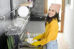 giovane donna felice che indossa guanti gialli che lava i piatti in cucina a casa foto