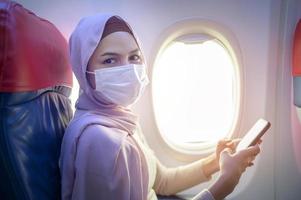 giovane donna musulmana con hijab che indossa una maschera facciale a bordo, nuovo viaggio normale dopo il concetto di pandemia covid-19 foto