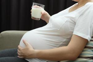 donna incinta che beve latte sul divano, sano per un nuovo concetto di famiglia. foto