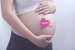 donna incinta che tiene il suo bambino non ancora nato con la carta del cuore, sano per la nuova famiglia foto