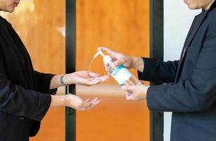 due uomini d'affari asiatici e una donna in abito nero si stanno lavando le mani con gel alcolico prima di entrare nella sala del seminario della riunione. foto