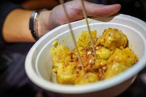 un gnocco giallo al vapore condito con aglio fritto messo nel bicchiere di carta. a bangkok, thailandia, cibo da strada colpito dal cibo. foto