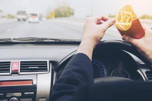 uomo d'affari che mangia patatine fritte e guida pericolosamente l'auto foto